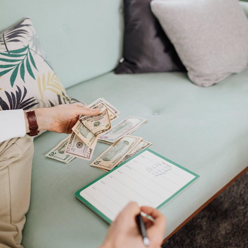 person writing on paper while holding money